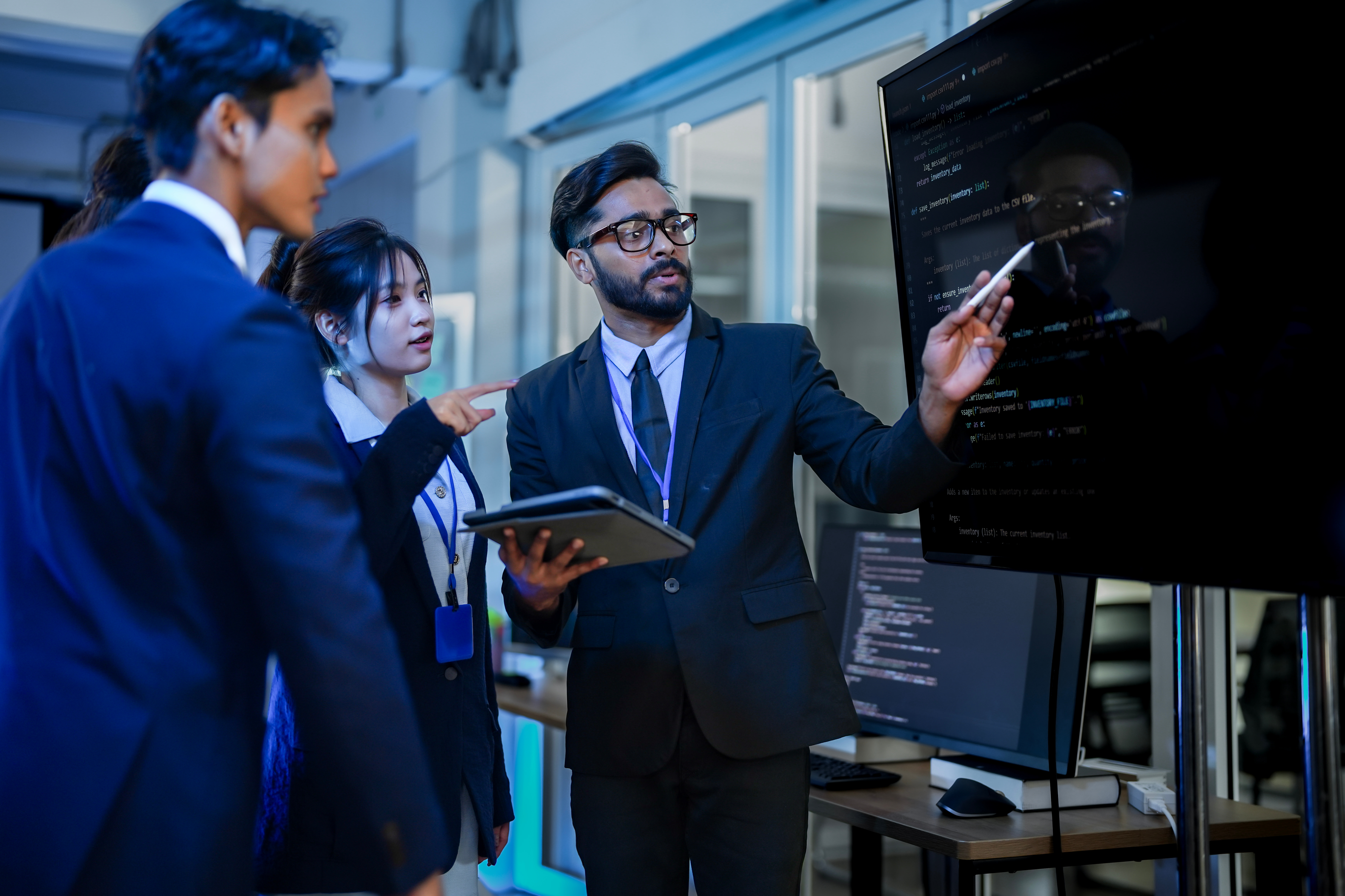 A senior software architect leads a code review session, explaining a complex algorithm to junior developers. He uses a stylus to highlight specific functions on the main display.